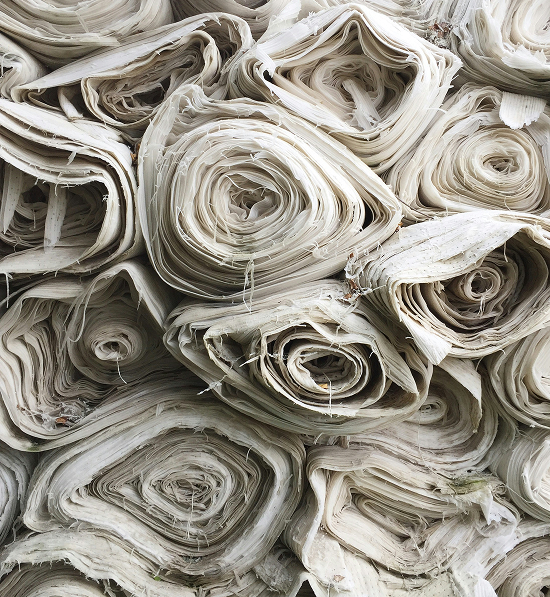 Rotoli di tessuto grezzo arrotolati, rappresentanti materiali tessili per progetti di sostenibilità nella moda.